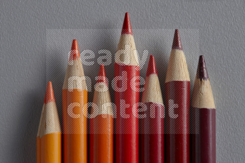 A collection of colored pencils arranged showcasing a gradient of orange and red hues on grey background