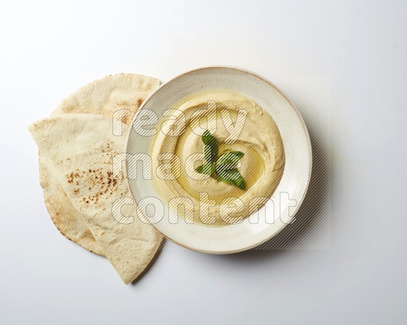 Hummus in a pottry plate garnished with mint  on a white background