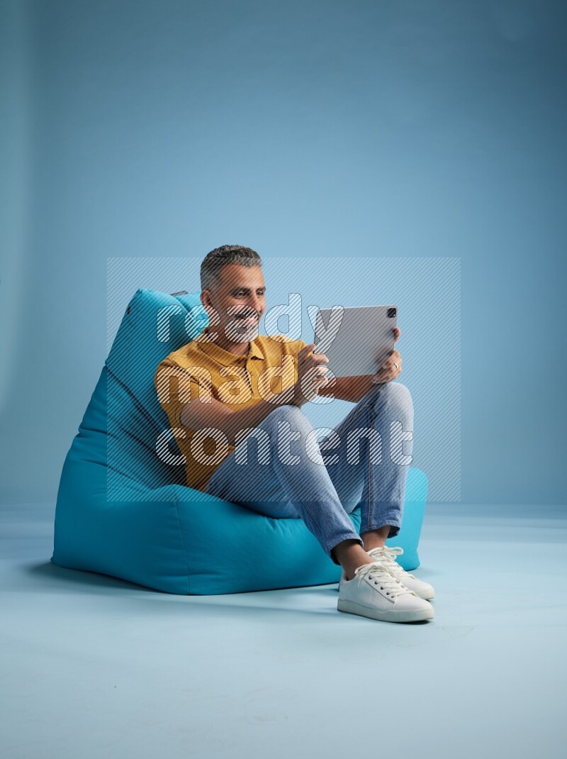 A man sitting on a blue beanbag and working on tablet