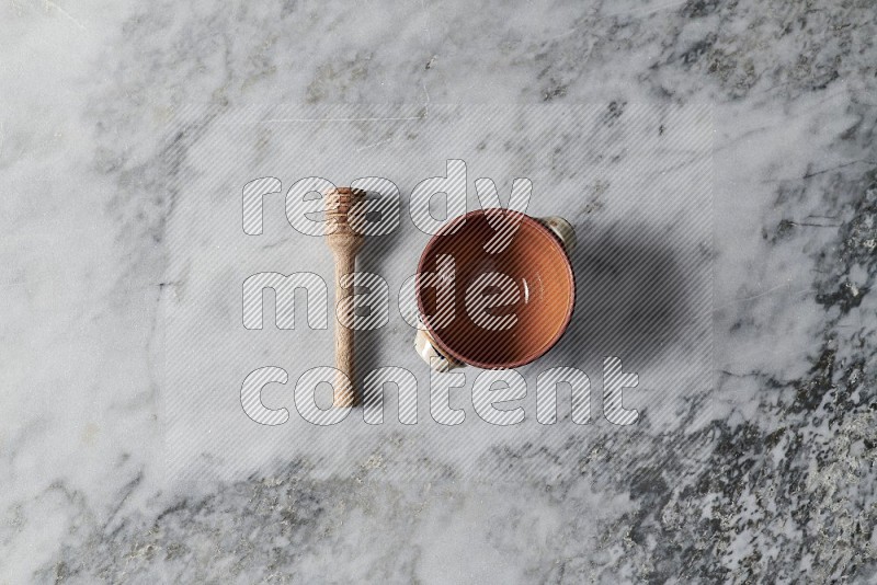 Brown Pottery Bowl with wooden honey handle on the side on grey marble flooring, Top view