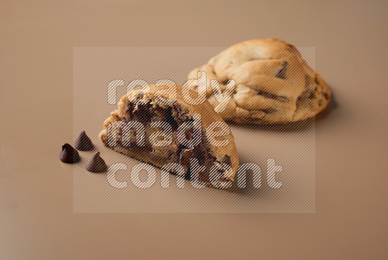 a chocolate chip cookie with another one cut in half on a brown background