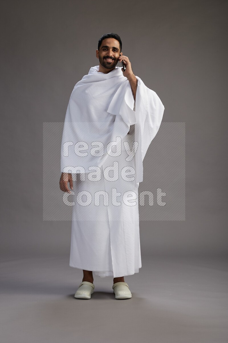 A man wearing Ehram Standing talking on phone on gray background