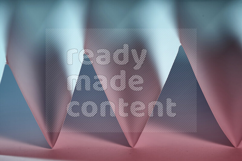 A close-up abstract image showing sharp geometric paper folds in blue and pink gradients