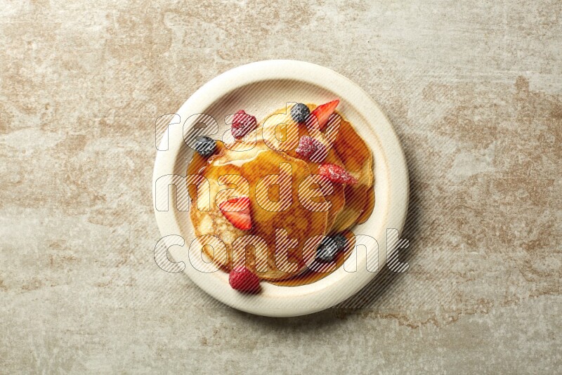 Three stacked mixed berries pancakes in a grey plate on beige background