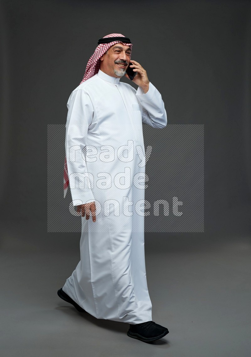 Saudi man with shomag Standing talking on phone on gray background