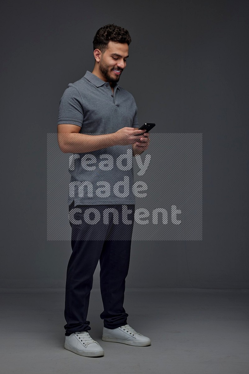 A man wearing casual standing and using his phone eye level on a gray background