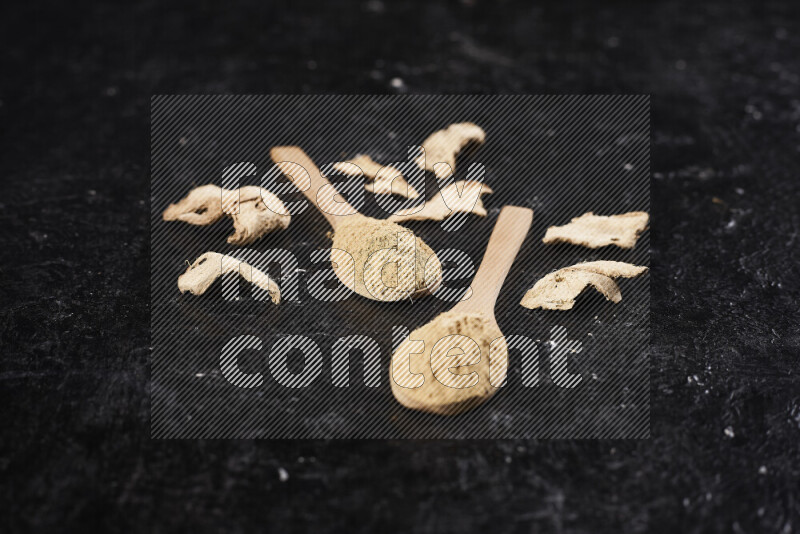 Two wooden spoons full of ground ginger powder on black background