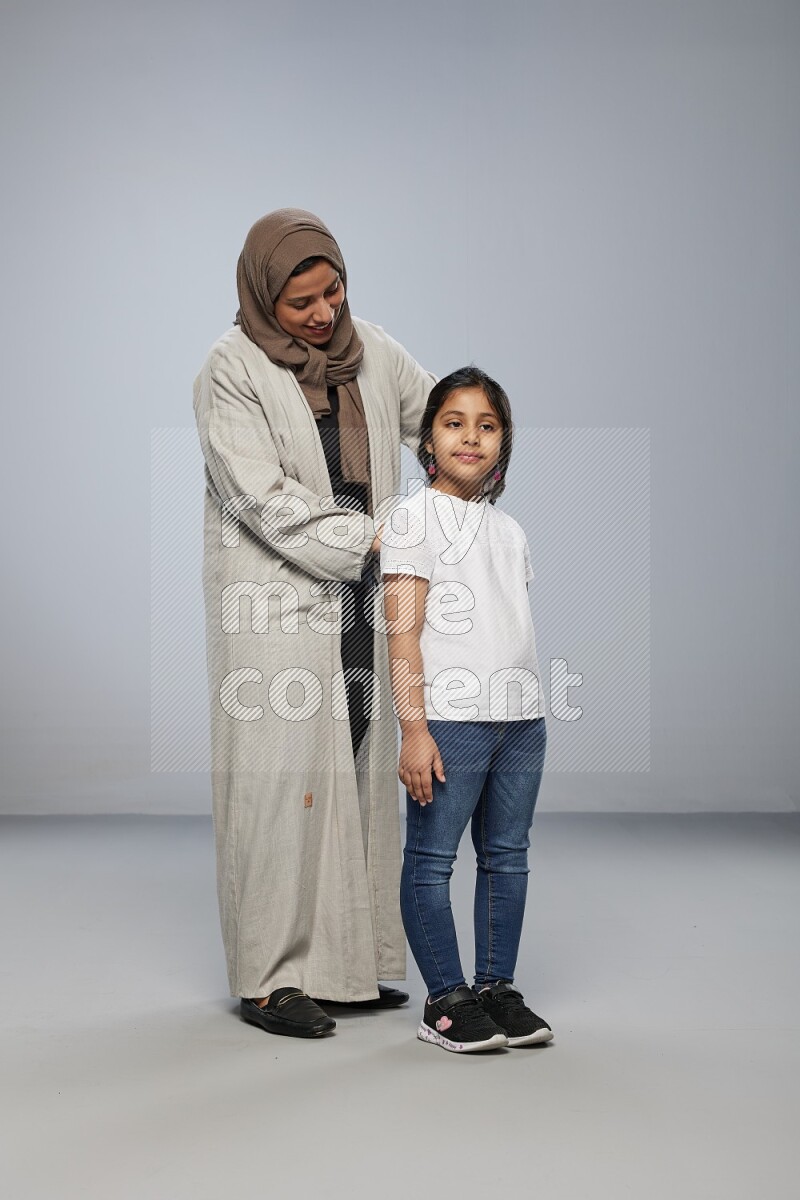 Mom standing styling hair for her daughter on gray background