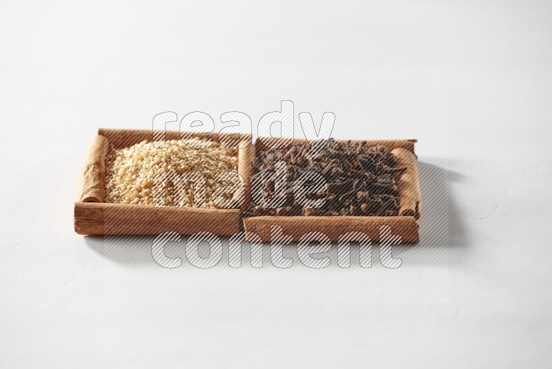 مربعان من أعواد القرفة ممتلئان بالقرنفل وبذور السمسم علي خلفية بيضاء