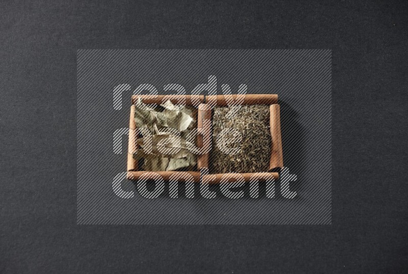 مربعان من أعواد القرفة ممتلئان بحبوب الكمون وأوراق الغار علي خلفية سوداء