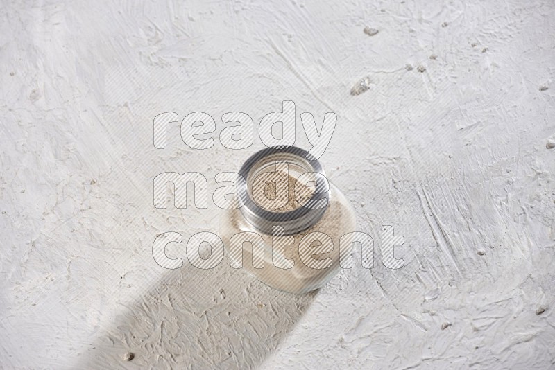 A glass spice jar full of garlic powder on a textured white flooring in different angles