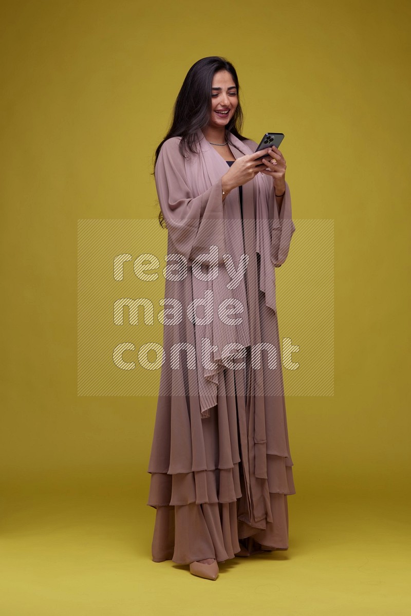 A woman Texting on a Yellow Background wearing Brown Abaya