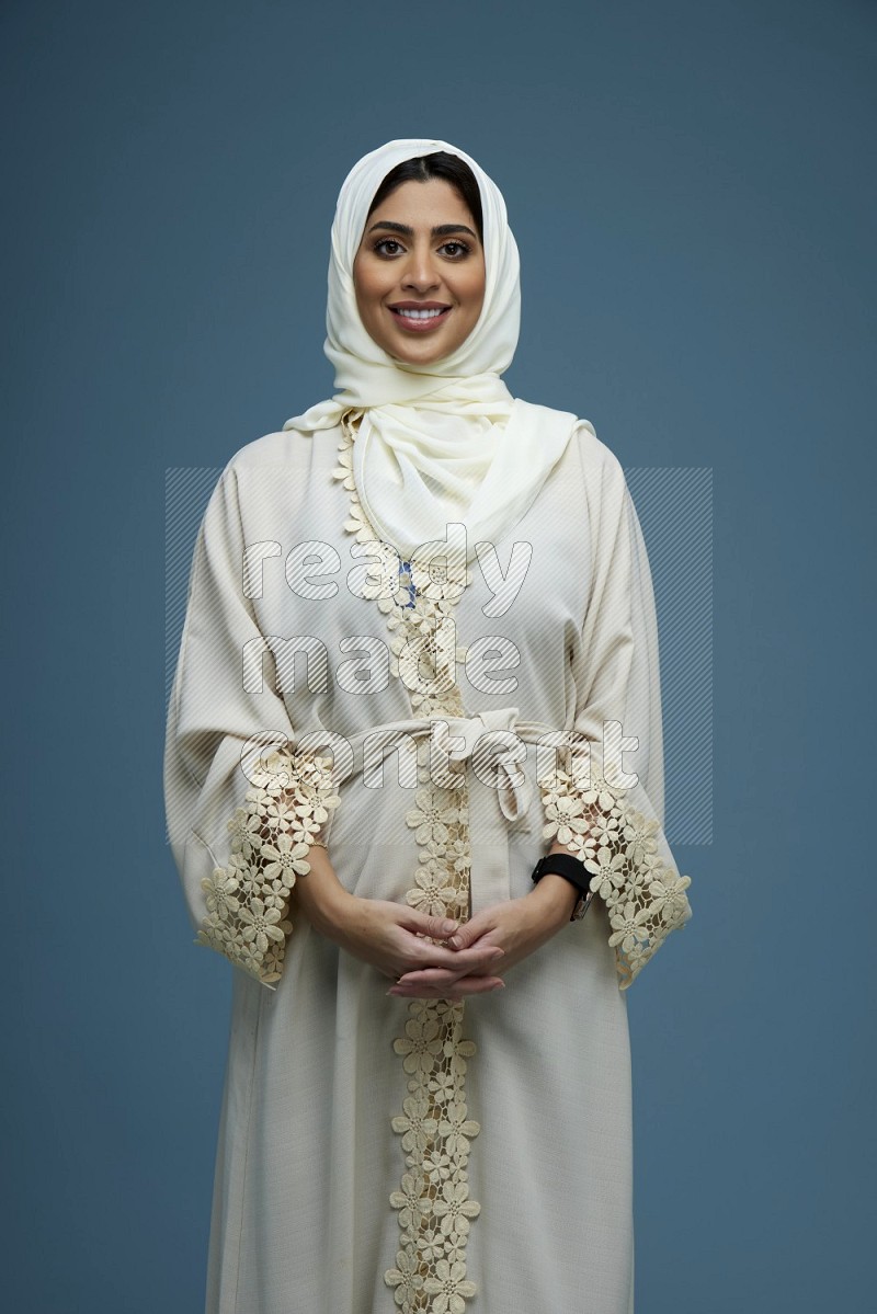 A Saudi woman posing in a blue background wearing off-white Abaya Hijab