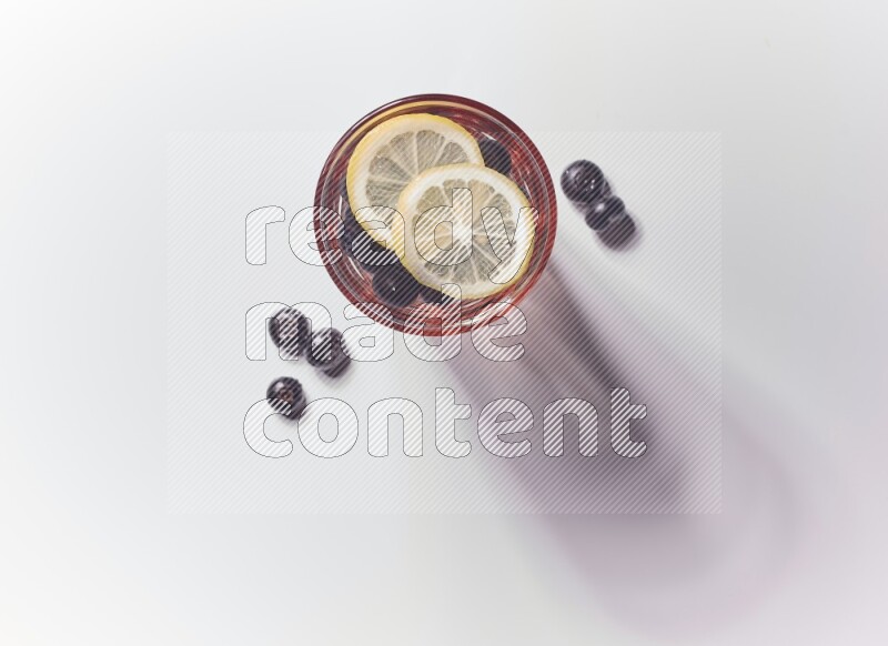 Blue transparent glass filled with blueberries decorated with lemon slices on a white background
