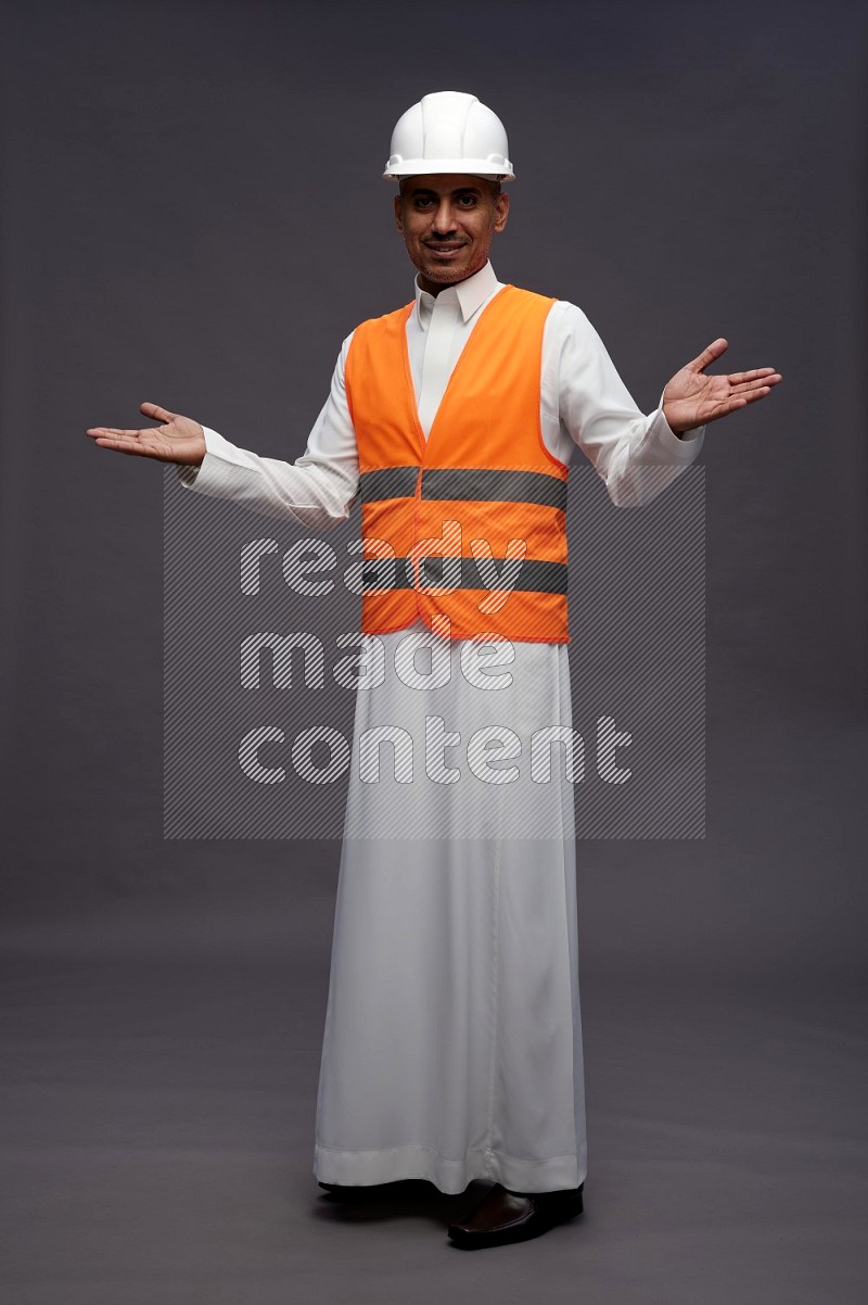 Saudi man wearing thob with engineer vest standing interacting with the camera on gray background