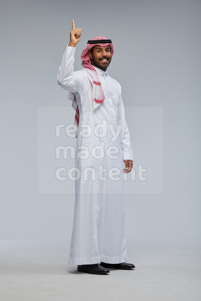 Saudi man Wearing Thob and shomag standing interacting with the camera on Gray background