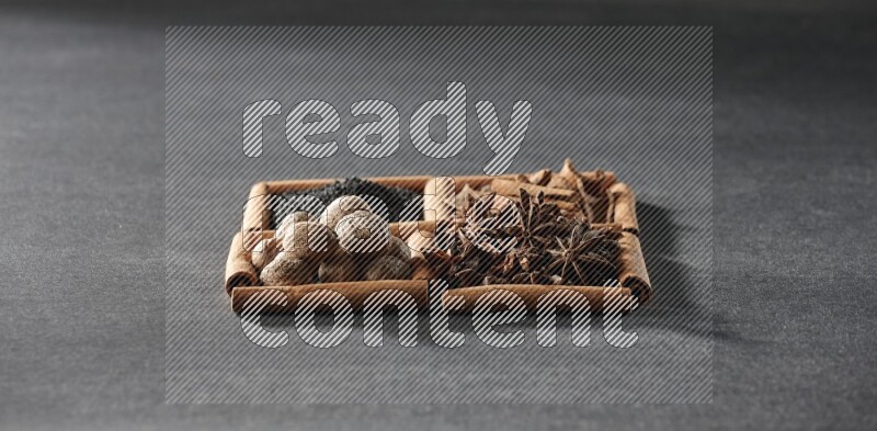 4 مربعات من عيدان القرفة ممتلئة بحبة البركة السوداء والقرفة واليانسون النجمي وجوزة الطيب على أرضية سوداء