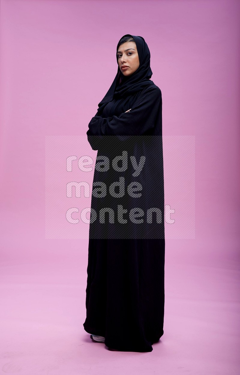 Saudi woman wearing Abaya standing with crossed arms on pink background