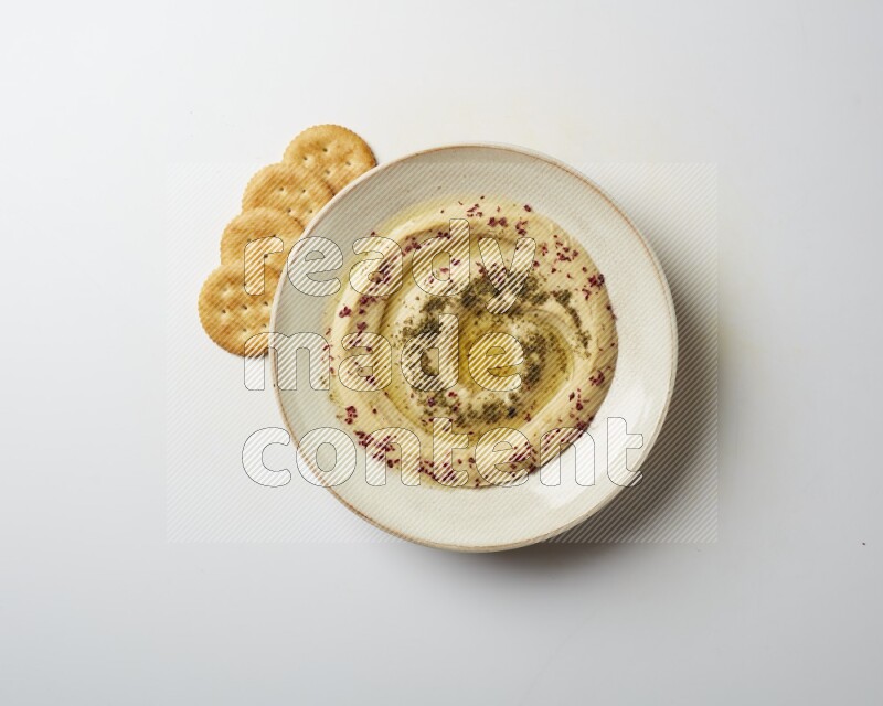 Hummus in a pottry plate garnished with zaatr & sumak on a white background