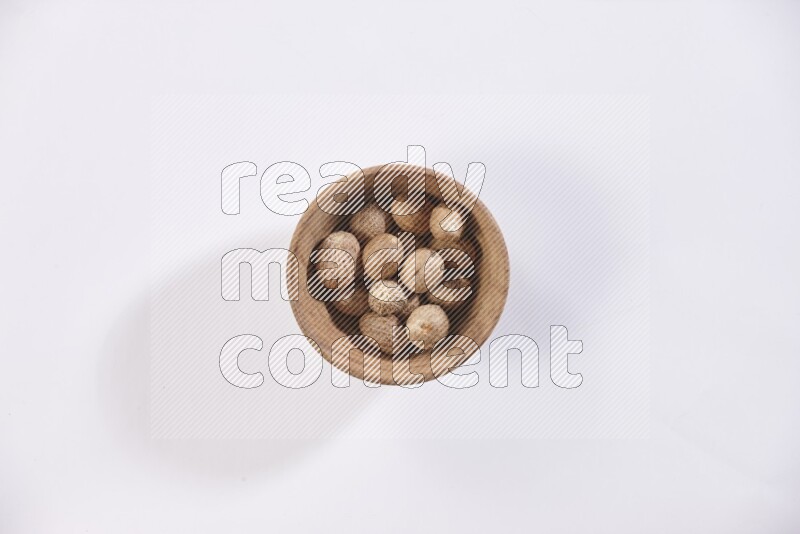 A wooden bowl full of whole nutmeg seeds on a white flooring