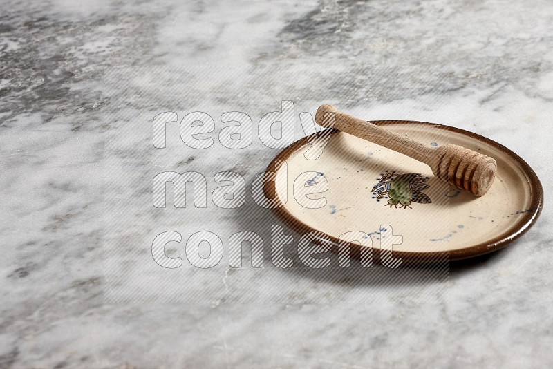 Decorative Pottery Plate with wooden honey handle in it, on grey marble flooring, 45 degree angle