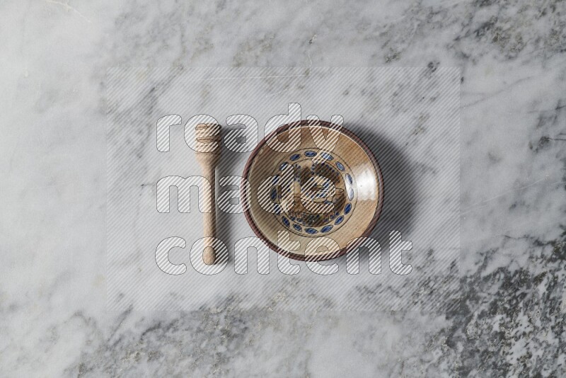 Decorative pottery plate with wooden honey dipper on the side on grey marble background
