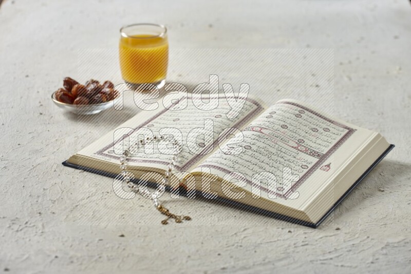 Quran with dates, prayer beads and different drinks all placed on textured white background