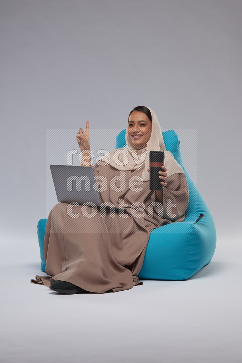 A Saudi woman sitting on a blue beanbag and working on laptop