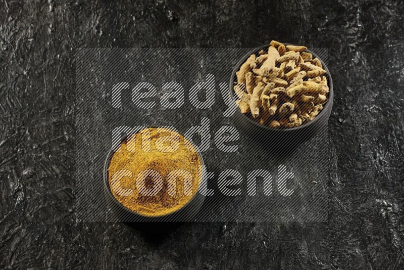 وعاءان من الفخار باللون الأسود، أحدهما ممتلئ ببودرة الكركم والآخر ممتلئ بأصابع كاملة من الكركم المجفف على خلفية سوداء