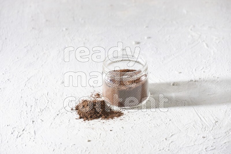 A glass jar full of cloves powder on a textured white flooring