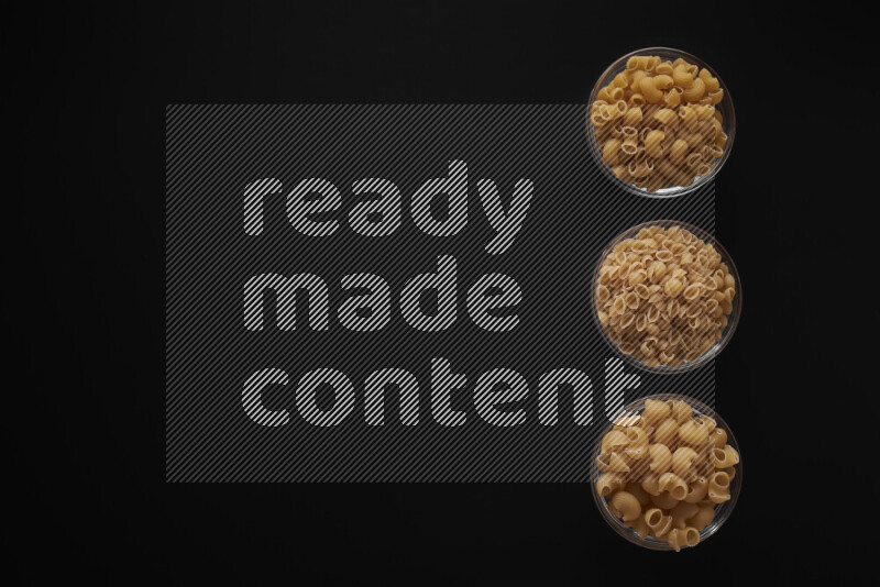 Different pasta types in 3 glass bowls on black background