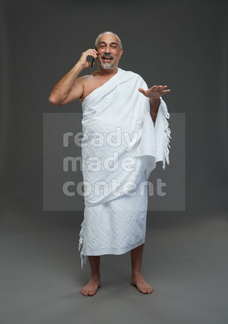 A man wearing Ehram Standing talking on phone on gray background