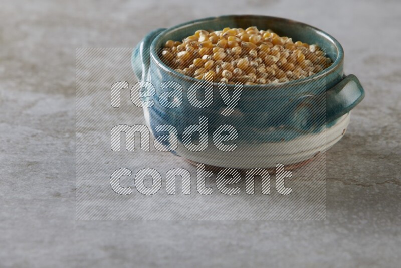 corn kernel in a multi-colored handheld ceramic bowl on a grey textured countertop