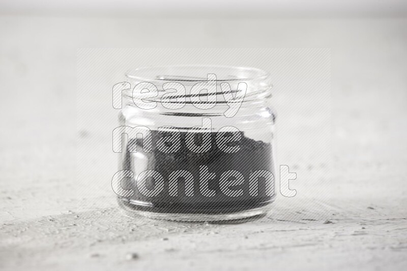 A glass jar full of black seeds on a textured white flooring