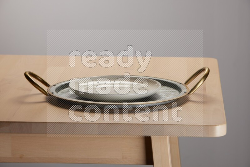 white plate placed on a rounded stainless steel tray with golden handels on the edge of wooden table