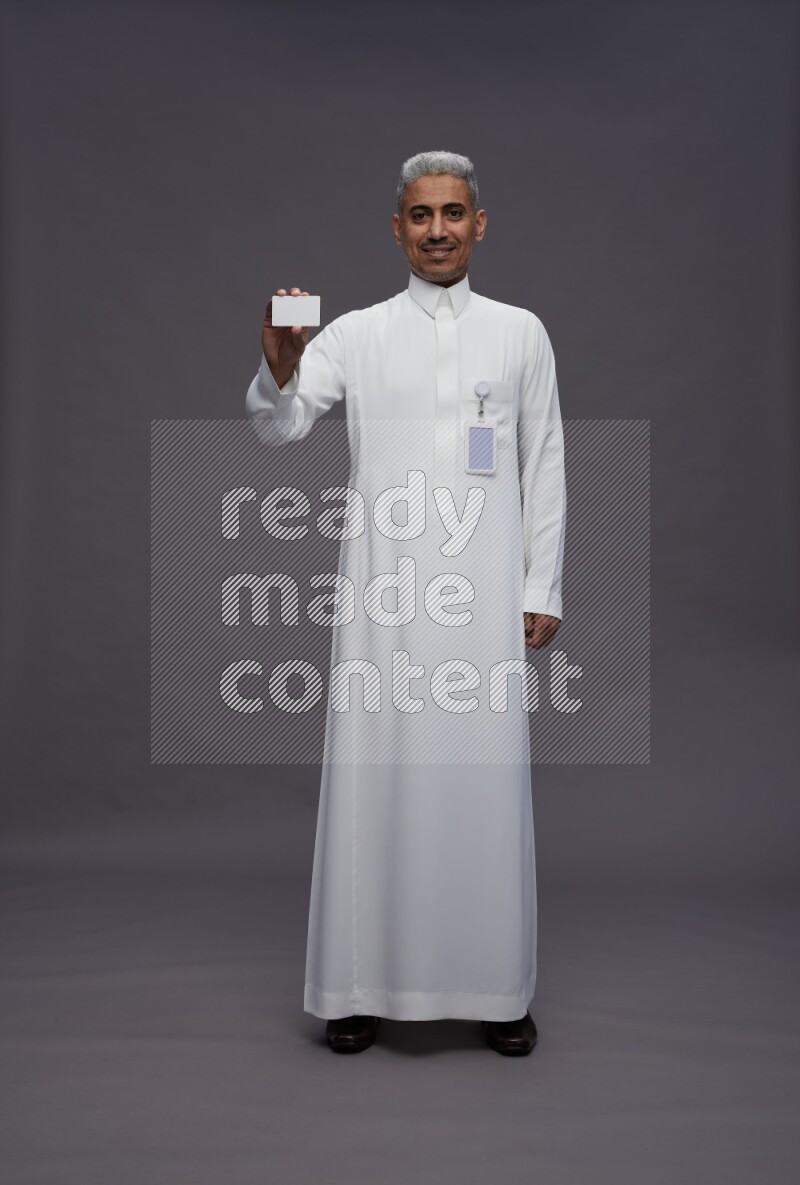 Saudi man wearing thob with pocket employee badge standing holding ATM card on gray background