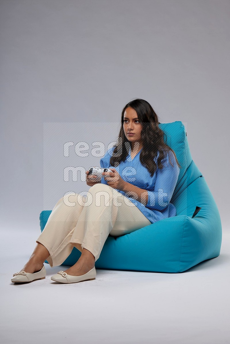 A woman sitting on a blue beanbag and gaming with joystick