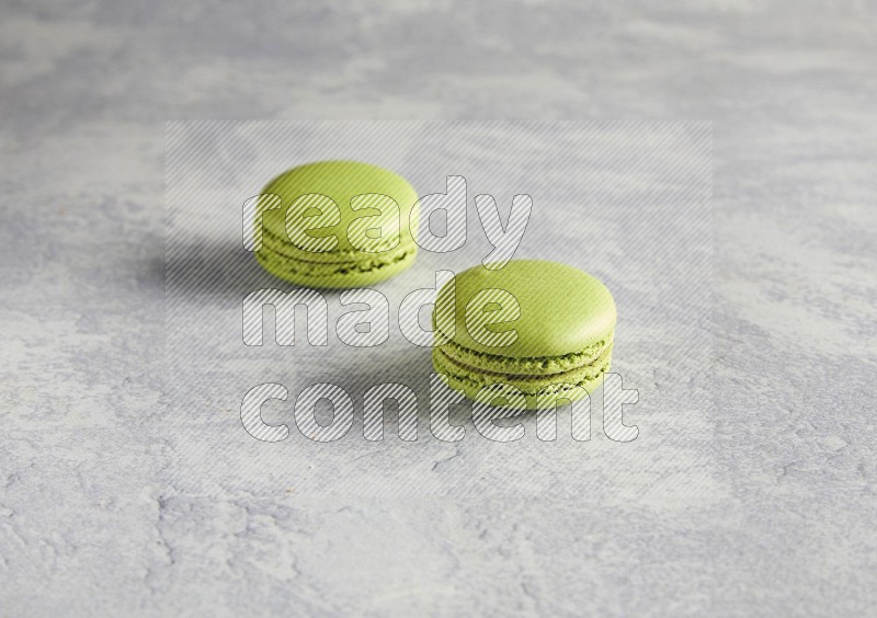 45º Shot of two Green Pistachio macarons  on white  marble background