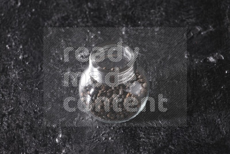 حبوب الفلفل الأسود في وعاء زجاجي علي خلفية سوداء