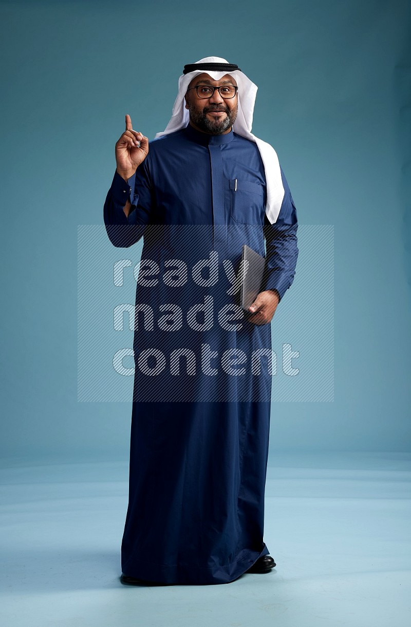 Saudi Man with shimag Standing working on laptop on blue background