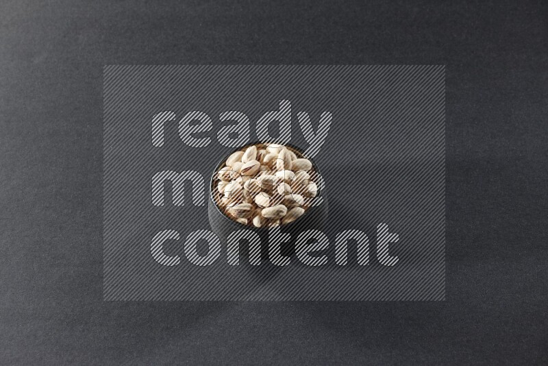 A black pottery bowl full of pistachios on a black background in different angles