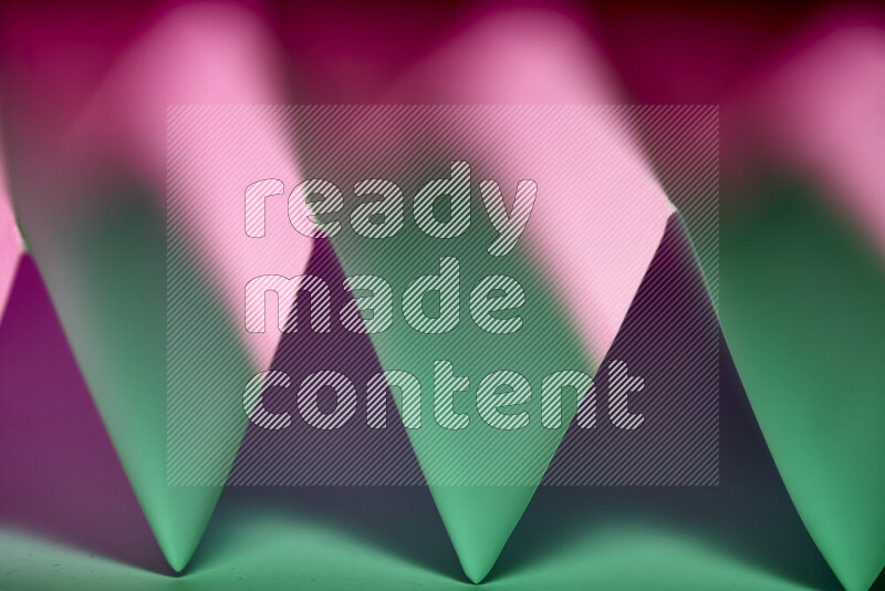 صورة مجردة مقربة تظهر طيات ورقية هندسية حادة بتدرجات اللون الأخضر والارجواني