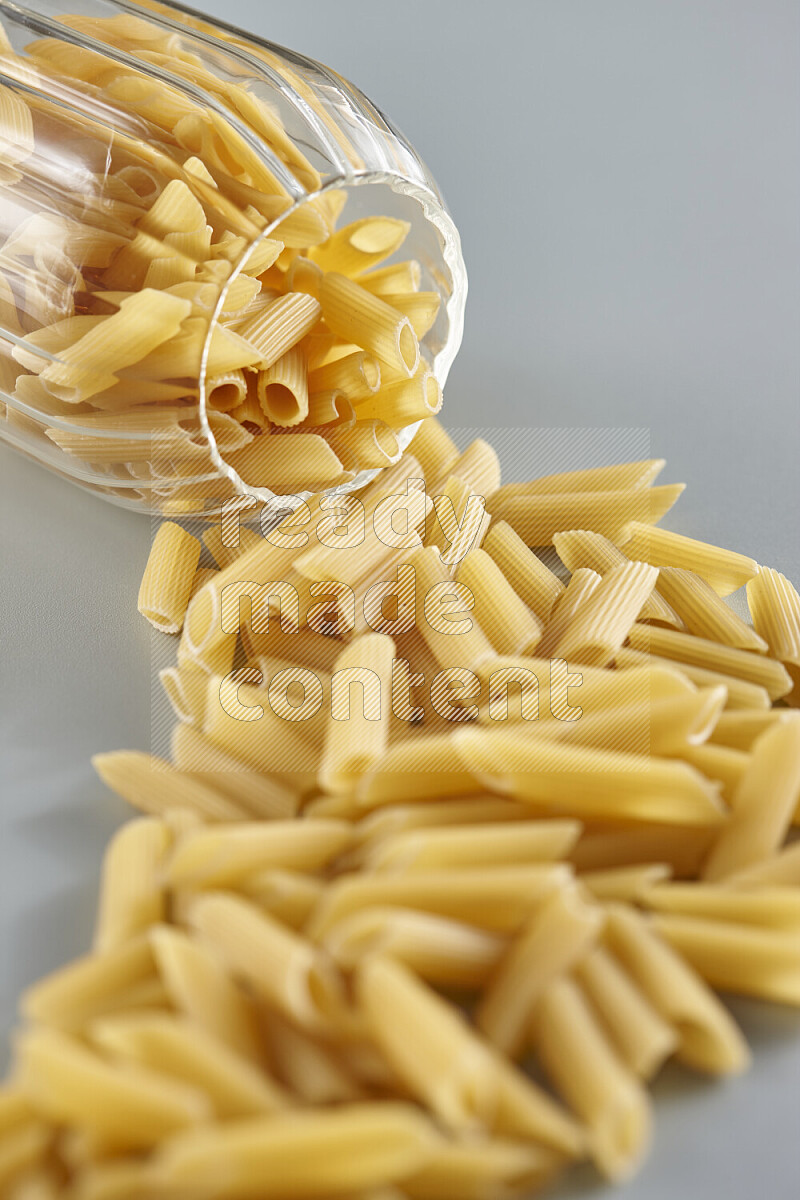 Flipped jar full of raw pasta on light blue background