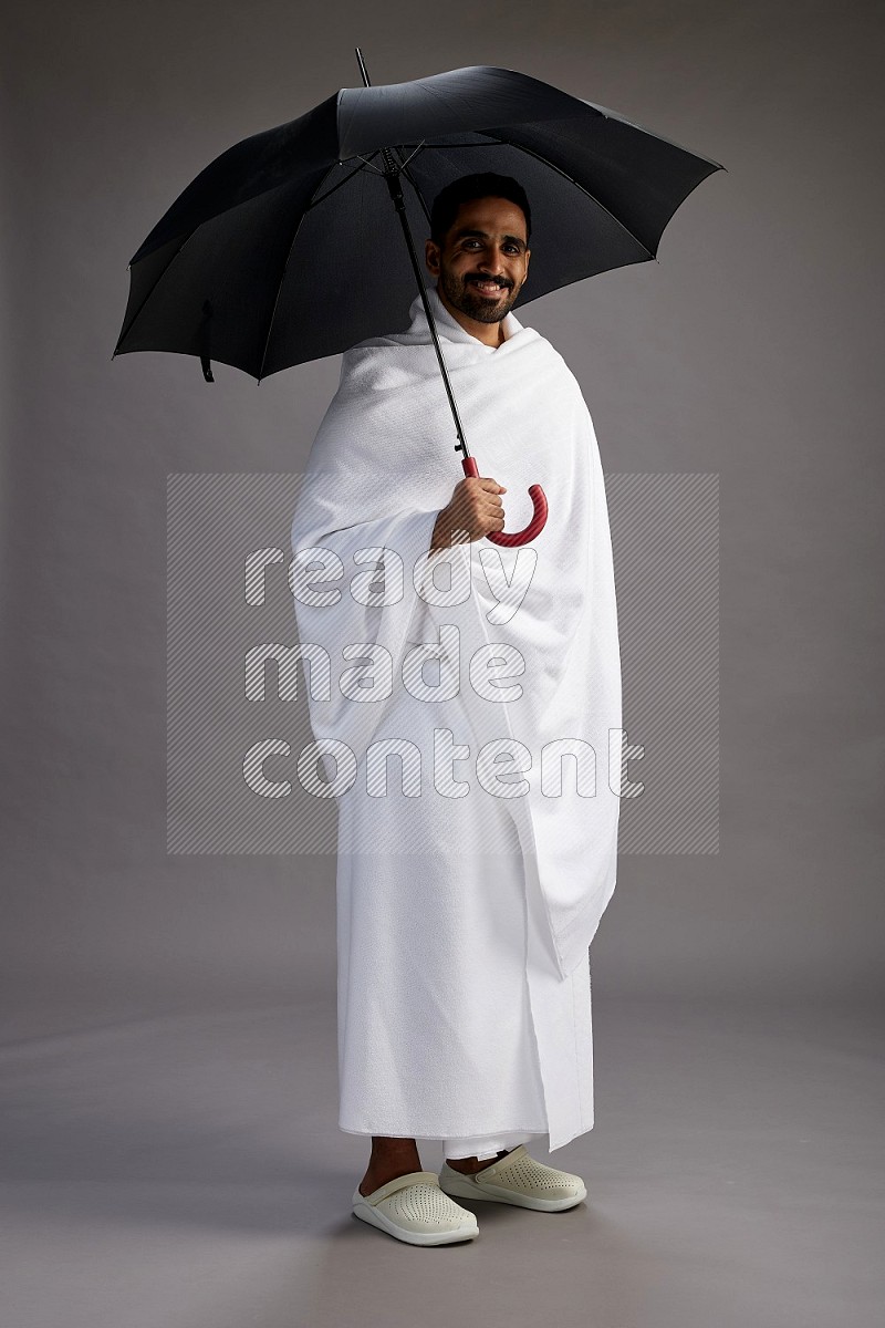 A man wearing Ehram Standing holding umbrella on gray background