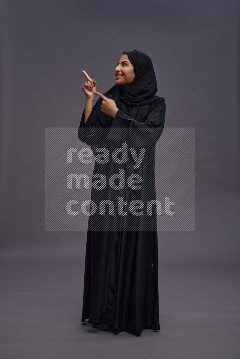 Saudi woman wearing Abaya standing interacting with the camera on gray background