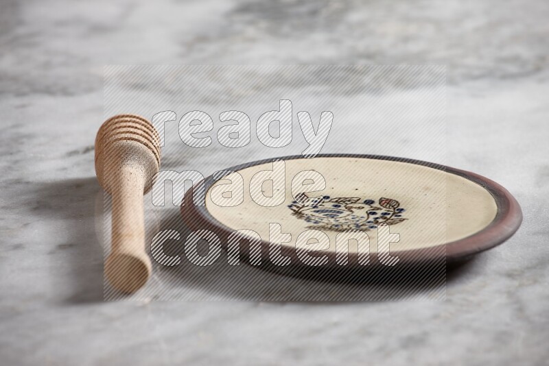 Decorative pottery plate with wooden honey dipper on the side on grey marble background