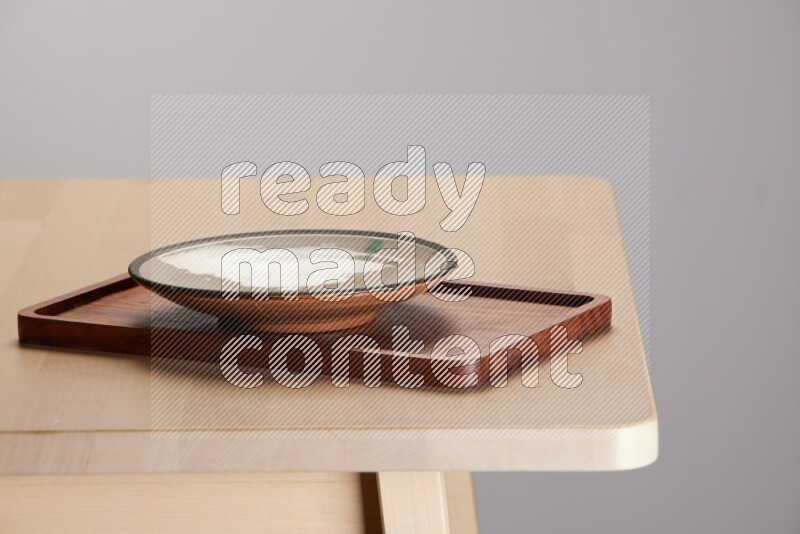 multi-colored pottery Plate placed on a rectangular wooden tray on the edge of wooden table