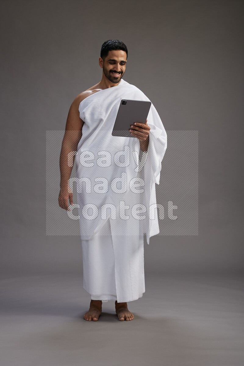 A man wearing Ehram and holding a tablet on gray background