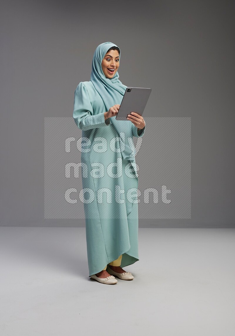 Saudi Woman wearing Abaya standing working on tablet on Gray background