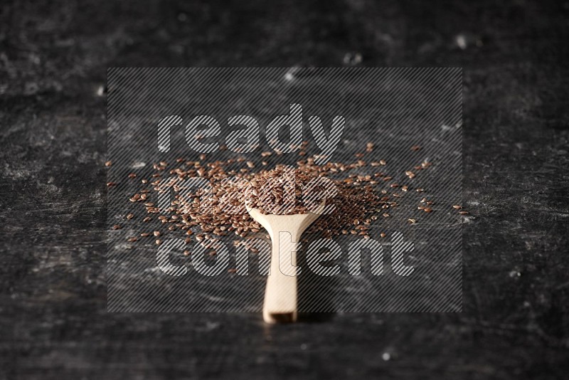 A wooden spoon full of flax and surrounded by seeds on a textured black flooring in different angles